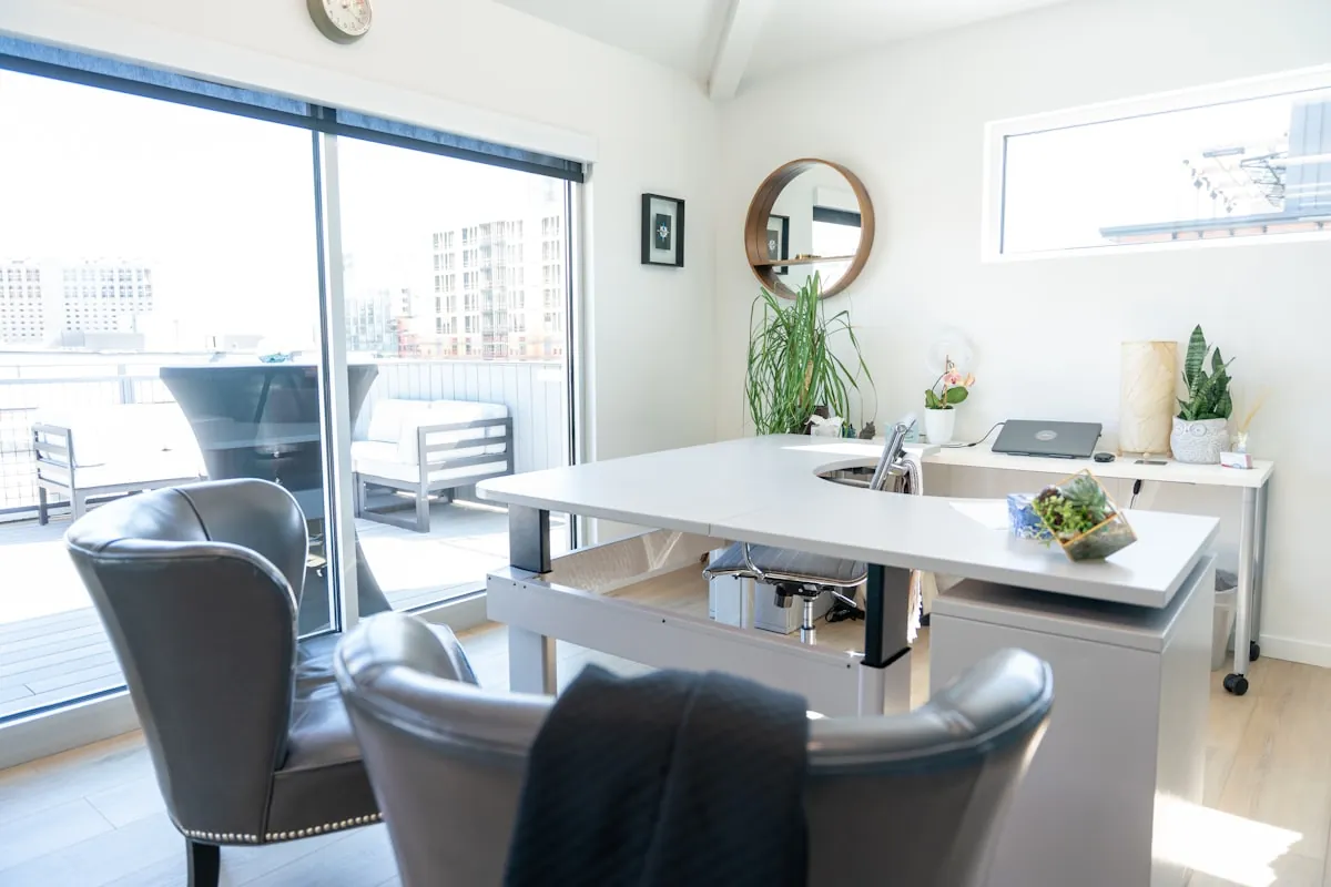 Bureau priv&eacute; lumineux avec un grand plan de travail blanc, deux fauteuils et une grande baie vitr&eacute;e