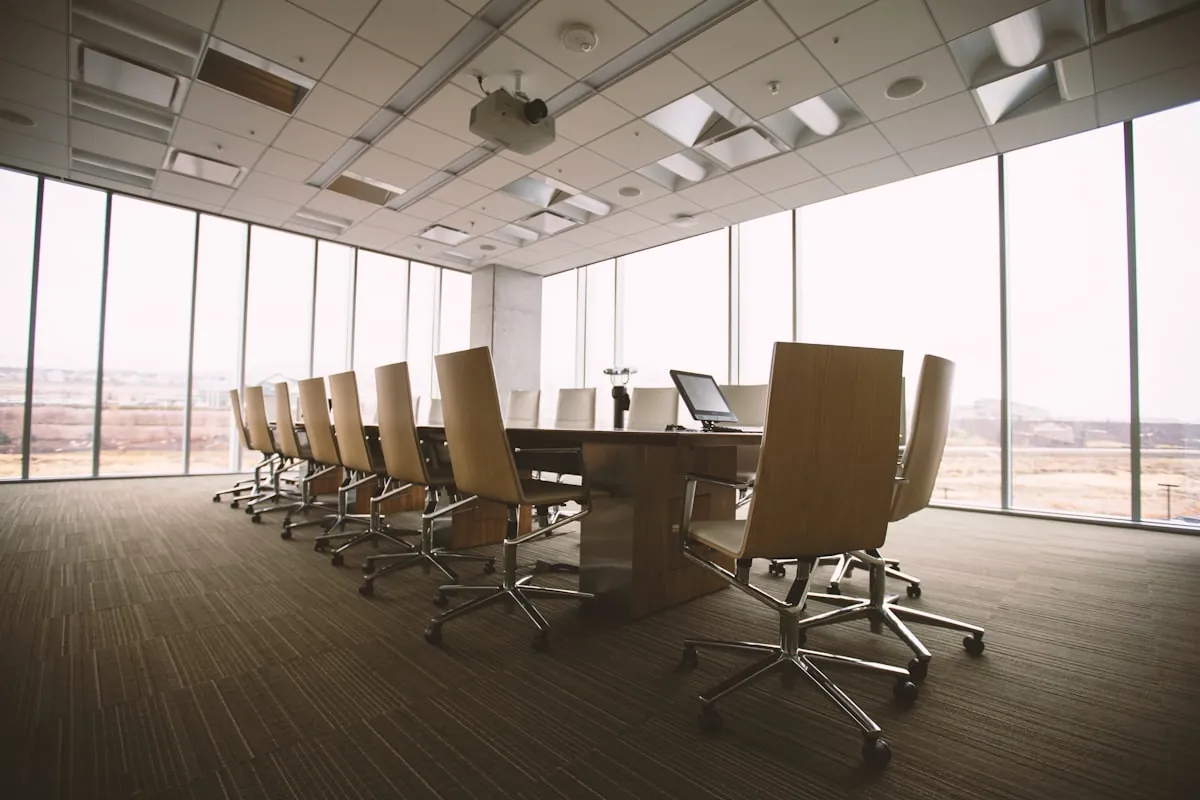 Salle de r&eacute;union avec une grande table de conf&eacute;rence, des fauteuils align&eacute;s et de larges baies vitr&eacute;es